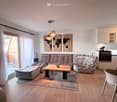modern living room with wooden floor, large windows, sliding glass door, sofa, coffee table, rug, pendant lights, world map wall art, kitchen with oven, dining table, chair