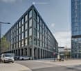 Modern office building with glass facade, multiple floors, cars parked outside, street lights, paved street