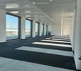 Empty office space with large windows, white walls, gray flooring, and ceiling lights.