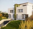 Modern white house, raised ground floor, multiple windows, green plants on the wall, driveway