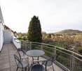 Balcony with table and chairs, metal railing, paved floor, view of trees and mountains