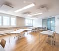 empty room, white walls, wooden floor, white tables and chairs, windows, ceiling lights