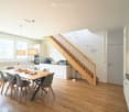 Dining room with wooden floor, dining table, chairs, kitchen with appliances, staircase