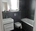 Bathroom with black tiles, white sink, white toilet, bathtub, mirror, window