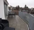 a balcony with tile flooring, metal railing, table and chairs, and distant cityscape