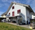 white 2-story house, red shutters, red roof, glass door, outdoor seating, solar panels, terrace, lawn, patio furniture