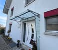House exterior, white facade, red trims, glass canopy, white door, brick pathway, potted plants