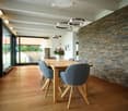 Dining room with wooden floor, large windows, dining table, chairs, brick wall, hanging lamps, flower vase