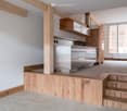 modern kitchen with stainless steel appliances, wooden cabinets, wooden flooring, white walls, large window