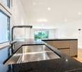 Modern kitchen with stainless steel sink, sleek faucet, and dark granite countertop. Large windows provide natural light, and the space features contemporary cabinetry.