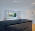 modern kitchen with black countertops, wooden floor, sliding glass doors, white walls, ceiling light