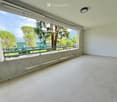Empty balcony with tiled floor, white walls, large window offering a view of trees and mountains, metal railing, and a light fixture on the ceiling.