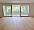Empty room with light wooden flooring and large sliding glass doors leading to a balcony.