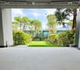 A spacious outdoor area with tiled flooring, surrounded by greenery and trees, with a modern building visible in the background.