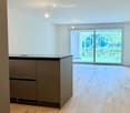 Empty room with light wooden flooring, white walls, and a small kitchen island with cabinets. Large sliding glass doors lead to an outdoor area.