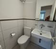 Bathroom with white tiles, toilet, sink, mirror, and a window