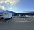 Empty parking lot with yellow lines, mountains in the background, a white trailer with a boat, and a building with a ladder.