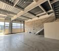 Empty warehouse space with concrete floor, metal staircase, large garage doors, and minimal equipment.