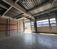 Empty garage with concrete floor, metal shelving units, large garage doors, and natural light from windows.