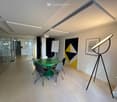modern office meeting room with glass walls, green table, white chairs, white board, artwork, floor lamp