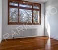 Empty room with wooden flooring, large windows with wooden frames, and a radiator below the windows.