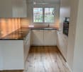 modern kitchen with white cabinetry, black countertop, wooden floor, white walls, stainless steel sink and faucet, integrated oven and microwave, large windows