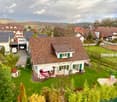 Detached house, brown roof, white walls, green shutters, driveway, garden, patio with furniture, car parked in garage
