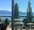 chairs and tables on balcony, green tablecloth, metal railing, view of mountains and lake