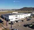White building, solar panels on the roof, parking lot with many cars, mountains in the background