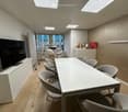 modern meeting room with a long white table, gray chairs, a flat screen TV, and a white cabinet