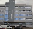 5 story building, grey exterior, large windows, multiple cars parked in front