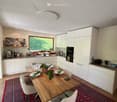 modern kitchen with dining area, wooden table, white cabinets, large window, red rug, modern lighting