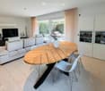 modern living room with white couch, wooden table, white chairs, TV, glass doors, white cabinets, tiled floor