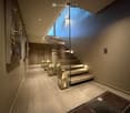 Modern hallway with sleek glass staircase, recessed lighting, and decorative lanterns placed along the floor.
