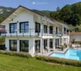 2 story house, white exterior, brown roof, large windows, balcony, swimming pool, green lawn, mountain view