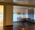 Dining room with wooden floor, white walls, dining table with red chairs, kitchen area with white cabinets, white tiled backsplash, and a ceiling fan.