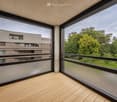 large balcony, large glass windows, wooden deck, modern building in background