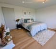 Bedroom with bed, rug, nightstand, plants, and framed pictures on the wall