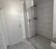 Modern bathroom with glass shower enclosure, white tiles, white door, towel rack, and toilet paper holder.