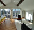 modern living room with wooden floor, large windows, balcony, white walls, black chair, white rug, black sofa, dining table, yellow chairs