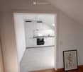 Empty room with white walls, wooden floor, white kitchen with oven and sink, picture frame on the wall