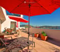 Terrace with lounge chairs, tables, chairs, and umbrellas, with a view of the city