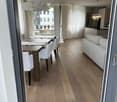 Furnished Room. Dining area with wooden table and chairs, a couch, and decorative lamps. The room has wooden floors and white curtains.
