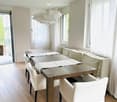 Furnished Room. Dining area with a wooden table, white chairs, and a white bench. The room has white walls, wooden floors, and white curtains.