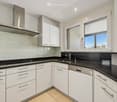 Kitchen. Modern kitchen with white cabinets, black countertops, stainless steel range hood, and a sink with a faucet.