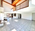 Empty room with white tiled floor, wooden ceiling, and white walls. There is a fireplace and a balcony with a wooden railing.