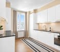 Modern kitchen with white cabinets, granite countertops, a sink with a gold faucet, and a built-in oven. A potted orchid sits on the counter, and a striped rug is on the floor.
