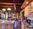 Kitchen. A kitchen with wooden cabinets, granite countertops, a sink, and a faucet. There is a table and chairs in the dining area, and a fireplace is visible. Appliances include a dishwasher, a blender, and a thermos. Various items are on the countertop,