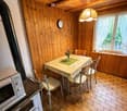 Dining area with wooden walls, tiled floor, dining table, chairs, microwave, stove, and a clock.