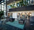 Modern, well-lit lobby area with dark tiled flooring, a green carpeted seating area, leather sofa and chairs, a glass coffee table, bar stools, and a reception desk.